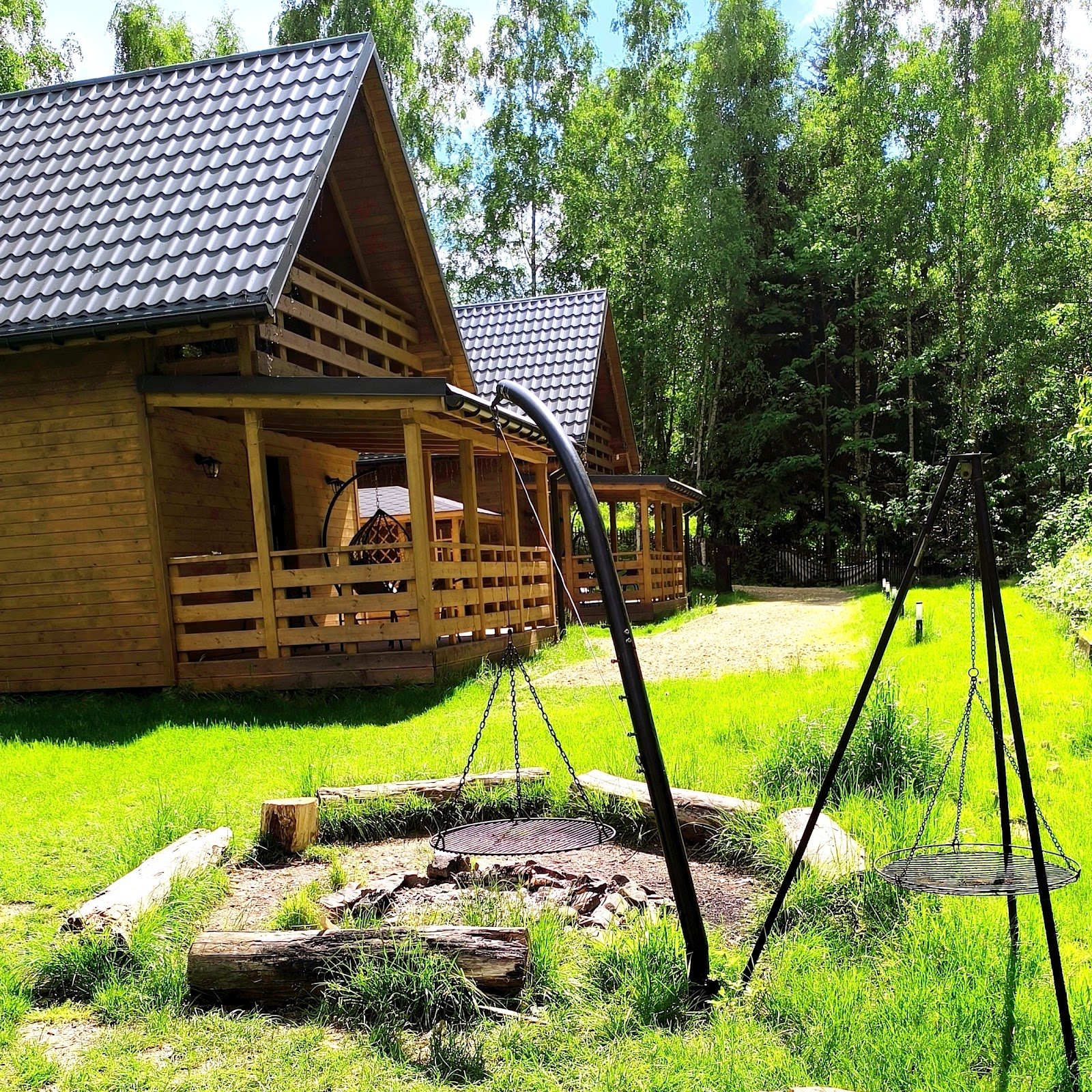 Palenisko z rusztem i grill na trójnogu na łące przed domkami latem